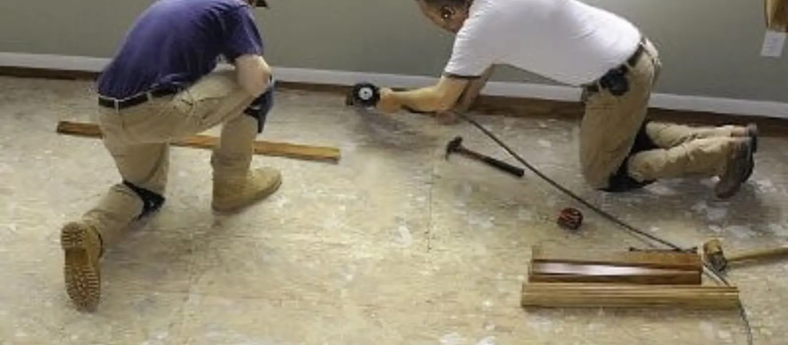 Two workers kneeling on a bare subfloor measuring and fitting new flooring